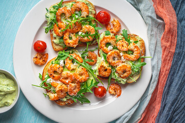 Toast or sandwiches with avocado oil, arugula and fried prawns on a white plate on a light blue background with a napkin. Healthy breakfast. View from above. Flat layout. Space for text.