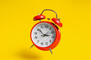 Red alarm clock in air on yellow background