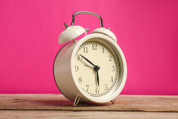 One white alarm clock on wooden table against bright pink background