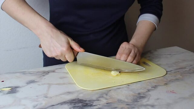 A person finely chops garlic on a cutting board. Medium shot. Spicy spicy food