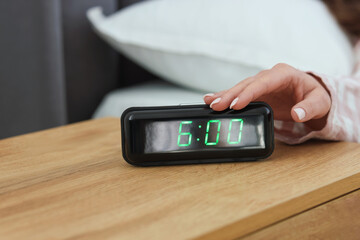 Woman turning off digital alarm clock on bedside table indoors, closeup