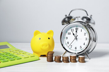Alarm clock, coins, calculator and piggy bank on white wooden table. Tax time