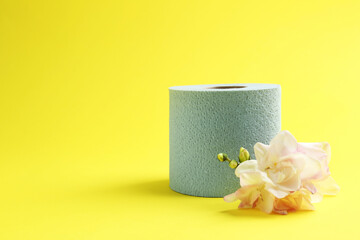 Light blue toilet paper roll and flowers on yellow background, space for text