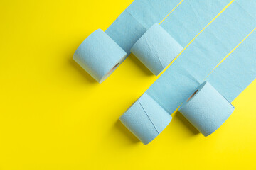 Light blue toilet paper rolls on yellow background, flat lay. Space for text