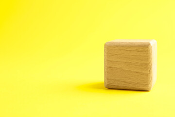 One wooden cube on yellow background, closeup. Space for text