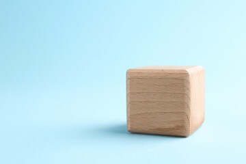 One wooden cube on light blue background, closeup. Space for text