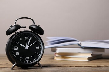 Time for knowledge. Alarm clock and books on wooden table, closeup. Space for text