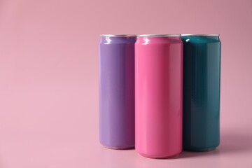 Colorful aluminium cans of beverage on pink background, space for text