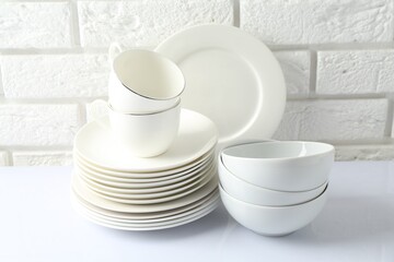 Different clean dishware on white table near brick wall