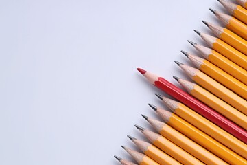 One red pencil among graphite ones on light grey background, top view. Space for text