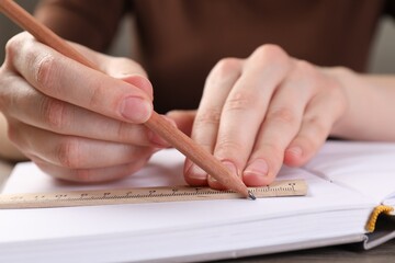 Woman drawing sketch with ruler and pencil on notebook at table, closeup