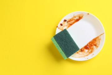 Dirty plate and sponge on yellow background, top view