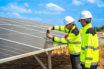 Two engineers wearing safety helmets and reflective jackets inspect a solar panel installation. One...