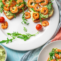 Healthy shrimp with avocado and arugula on toast for breakfast on a white plate on a light blue background. View from above. Flat layout.