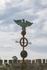 An ancient Roman eagle, covered with rust and patina, against a cloudy sky