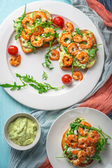 Healthy shrimp with avocado and arugula on toast for breakfast on a white plate on a light blue background. View from above. Flat layout.