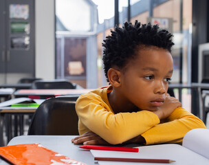 In school, thoughtful child resting head on desk, surrounded by books and pencils