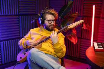 A focused male musician fine-tunes a guitar against the backdrop of a digital sound editing setup...