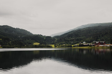 Norwegian fjord mountain landscape with a lake in the foreground and wooden houses on the shore. Overcast autumn day.