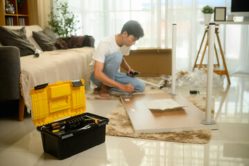 Focused young asian man assembling new furniture in his living room