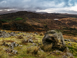 Rough textured boulder, sparse grasses, rolling hills under a cloudy sky.