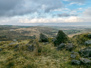 Obraz premium Rural setting. Large gray rocks dominate a hilltop. Fields and distant horizon under cloudy skies.