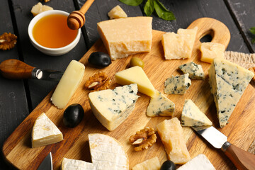 Board with different types of tasty cheese and honey on dark wooden background, closeup