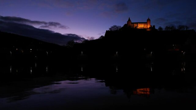 Amazing view of the Fortress Marienberg in W&uuml;rzburg, Germany. Bavarian castle with yellow evening lights in blue hour with beautiful reflections on the calm River Main in the foreground.