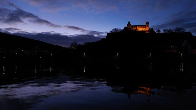 Amazing view of the Fortress Marienberg in W&uuml;rzburg, Germany. Bavarian castle with yellow evening lights in blue hour with beautiful reflections on the calm River Main in the foreground.