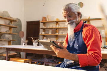 Elderly man in pottery studio using tablet, exploring creative ideas, copy space