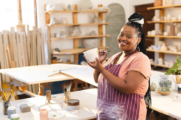 Smiling woman in pottery studio holding clay pot, enjoying creative process, copy space