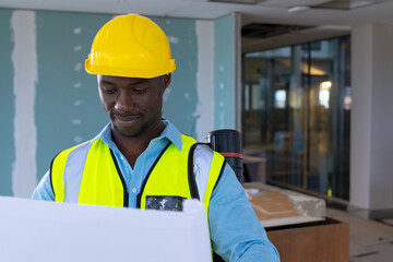 Reviewing blueprints, African American engineer wearing safety gear at construction site, copy space