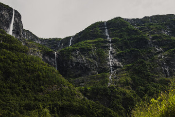 Norwegian fjord mountain landscape with green coniferous trees and waterfalls on the mountain flowing into the river.