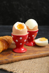 Holders with boiled chicken eggs and croissant on black background