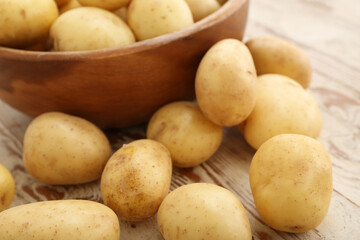 Bowl with raw potatoes on white wooden background
