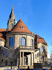 Fototapeta premium Historische Kirche mit markantem roten Ziegeldach und großen Fenstern an einem klaren Wintertag. Architekturaufnahme bei Tageslicht mit klarem Himmel.
