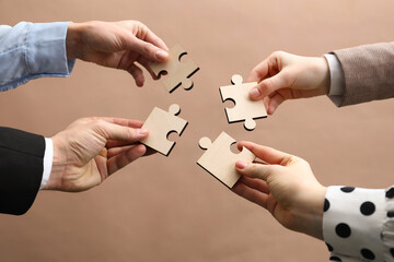 Teamwork. Group of people putting puzzle pieces together on beige background, closeup