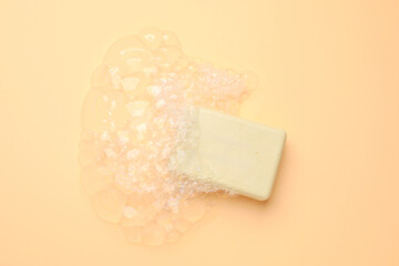 Soap bar with foam on peach background, top view