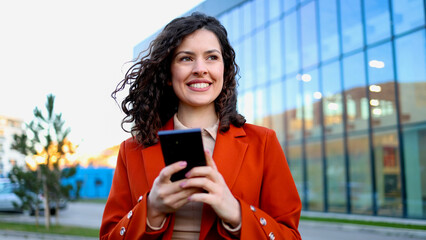 Smiling businesswoman using smartphone near office building