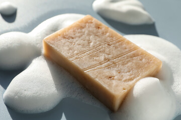 Soap bar with foam on grayish blue background, closeup