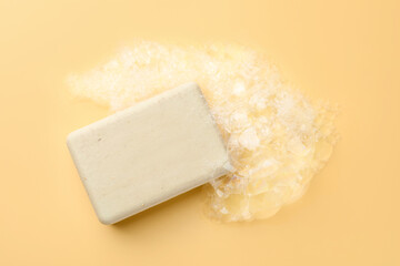 Soap bar with foam on yellow background, top view