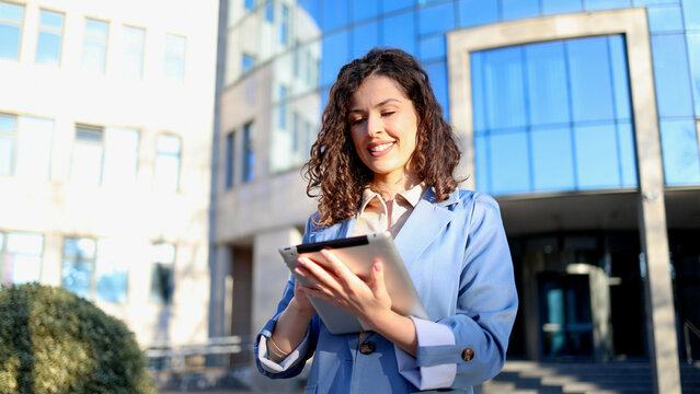 Smiling businesswoman using digital tablet outside office building