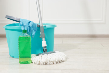 String mop, detergent, bucket and gloves on wooden floor near white wall. Space for text