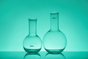 Empty flasks on mirror surface against green background. Laboratory equipment