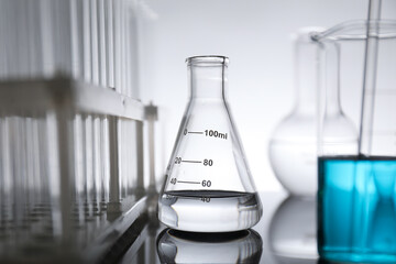Laboratory glassware with liquid on mirror surface against light background