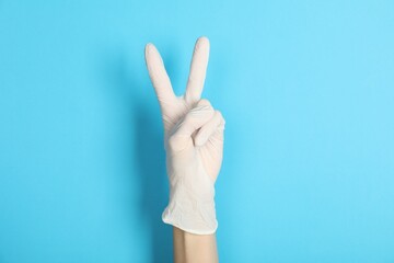 Doctor in medical glove showing two fingers on light blue background, closeup