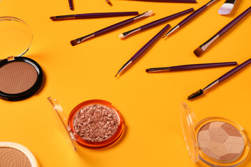 Makeup brushes and different decorative cosmetics on orange background