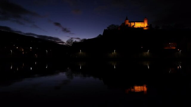 Bavarian castle with yellow evening lights in blue hour with beautiful reflections on the River Main in the foreground. Amazing real time footage of the Fortress Marienberg in W&uuml;rzburg, Germany.