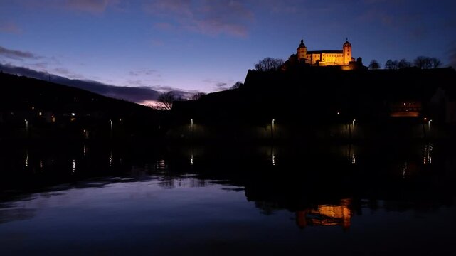 Amazing view of the Fortress Marienberg in W&uuml;rzburg, Germany. Bavarian castle with yellow evening lights in blue hour with beautiful reflections on the calm River Main in the foreground.