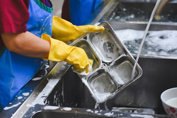 A woman is washing a stainless steel food tray.